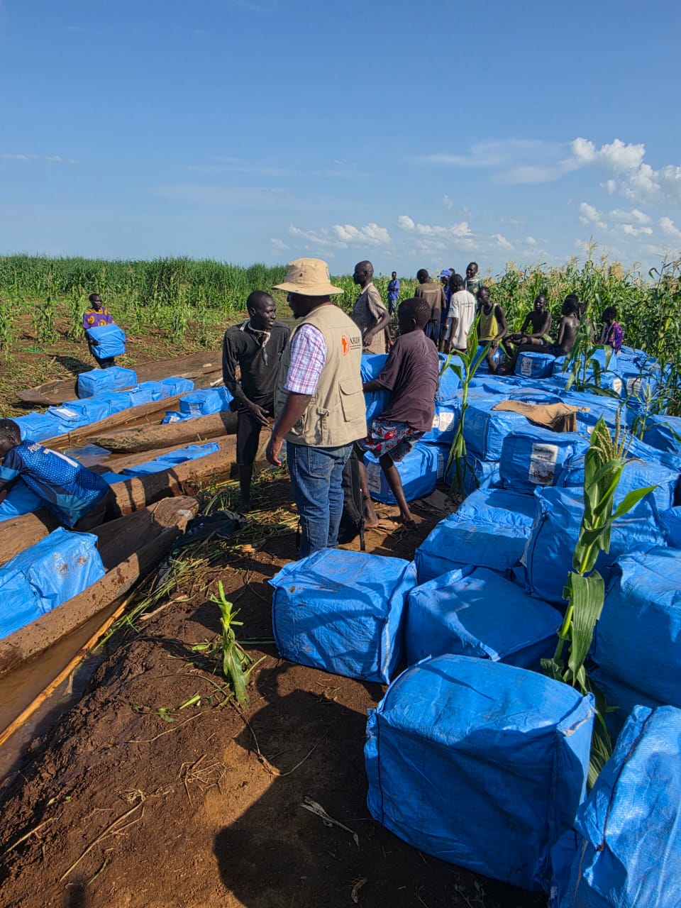 An ARDF team member and community members among stacked bales of mosquito nets in a flooded maize field in Ulang.